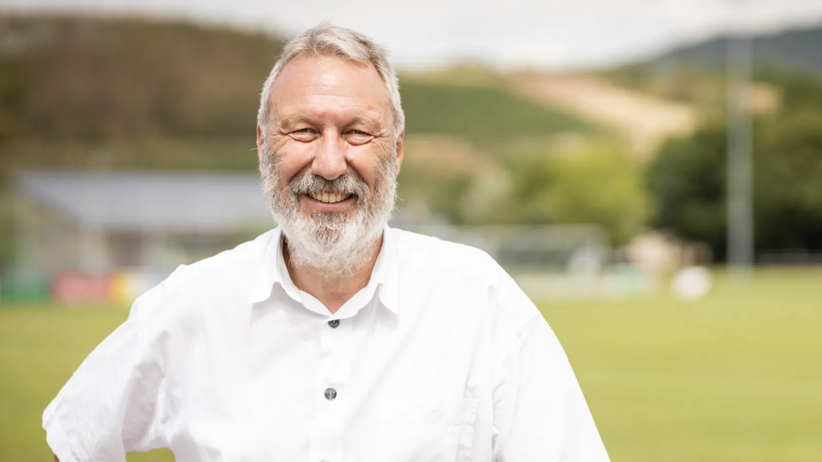 Ein lächelnder Mann vor dem Hintergrund eines dörflichen Fußballplatzes