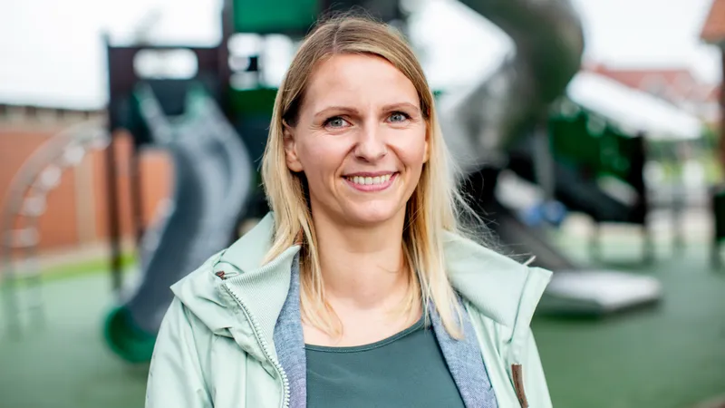 Eine lächelnde junge Frau vor dem Hintergrund eines Spielplatzes