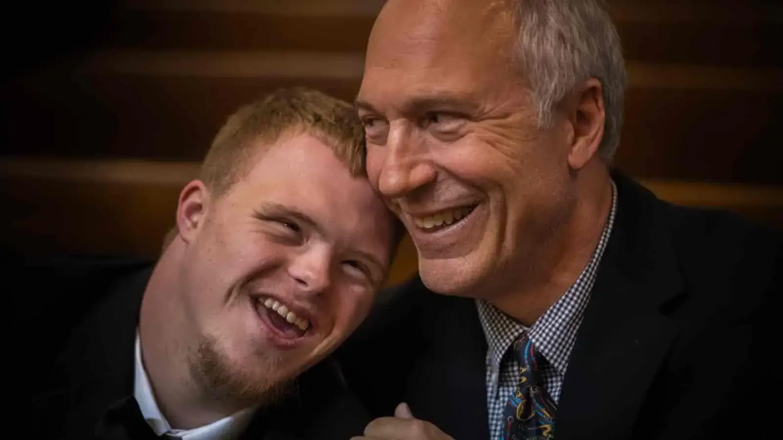 Portrait eines älteren und jüngeren Manns. Sie sind festlich gekleidet und lachen.