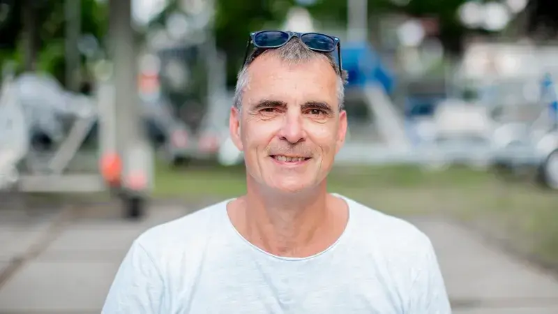 Ein Mann mittleren Alters in einem weißen T-Shirt auf der Straße blickt in die Kamera
