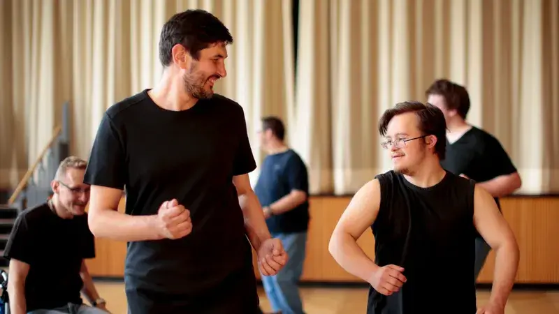 Ein Trainer und ein junger Mann mit Down Syndrom beim Üben eines Tanzes.