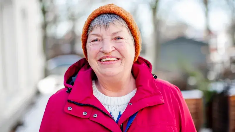 Eine ältere Frau mit Winterjacke und Mütze im Freien. Sie lächelt in die Kamera.