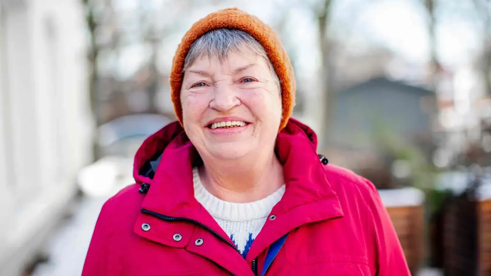 Eine ältere Frau mit Winterjacke und Mütze im Freien. Sie lächelt in die Kamera.