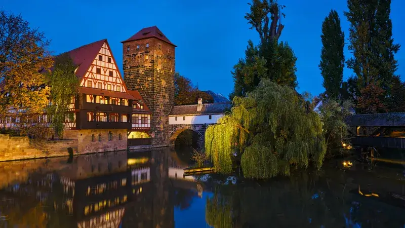 Eine Altstadt mit einem kleinen Fluss im Vordergrund bei Nacht.