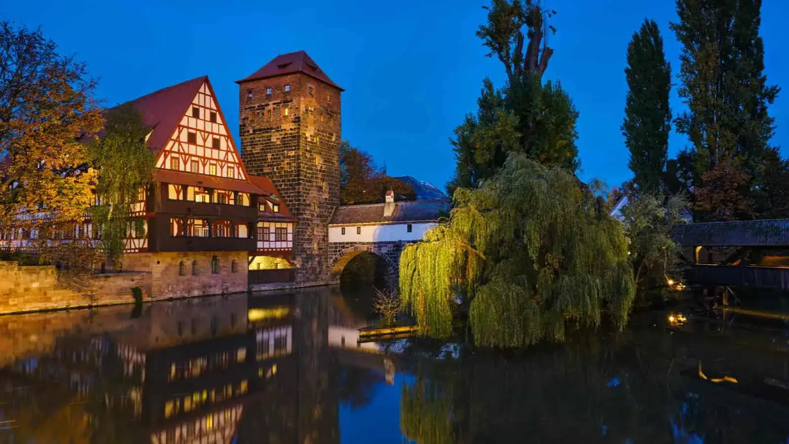 Eine Altstadt mit einem kleinen Fluss im Vordergrund bei Nacht.