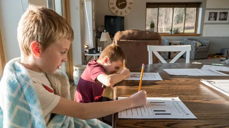 Zwei Jungen sitzen im Wohnzimmer und machen Hausaufgaben.