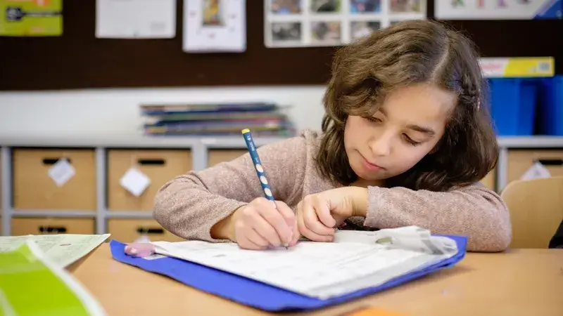 Ein Mädchen sitzt an einem Schreibtisch und schreibt mit einem Stift in ein Heft.
