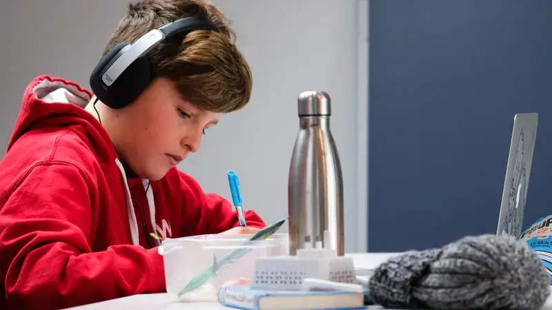 Ein Junge mit Kopfhörer macht Hausaufgaben am Schreibtisch