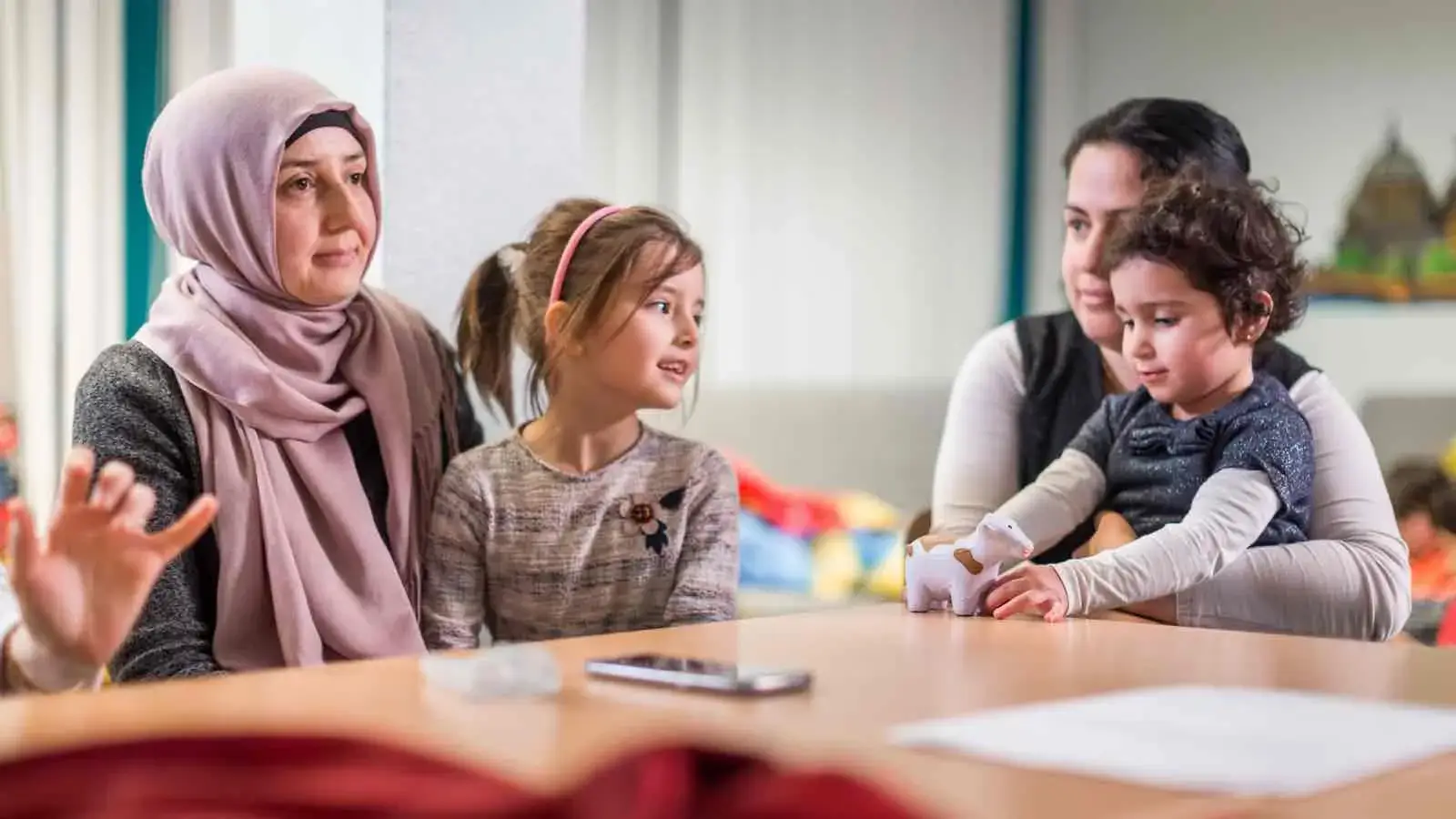 Zwei Frauen, eine davon mit Kopftuch, und zwei Kindern an einem Tisch