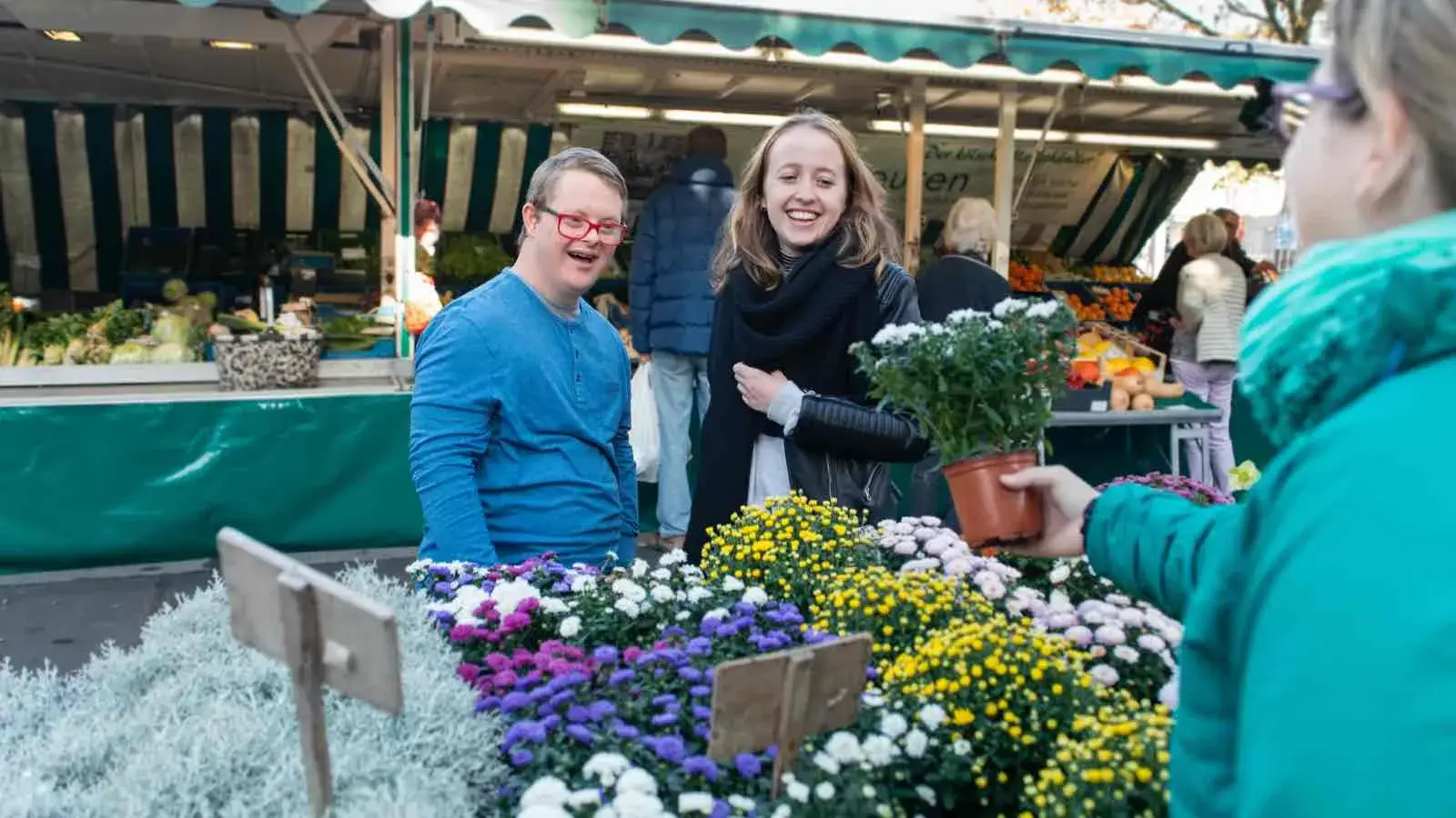 Zwei Jugendliche, ein Mädchen und ein Junge mit Down Syndrom auf einem Markt beim Einkauf von Blumen