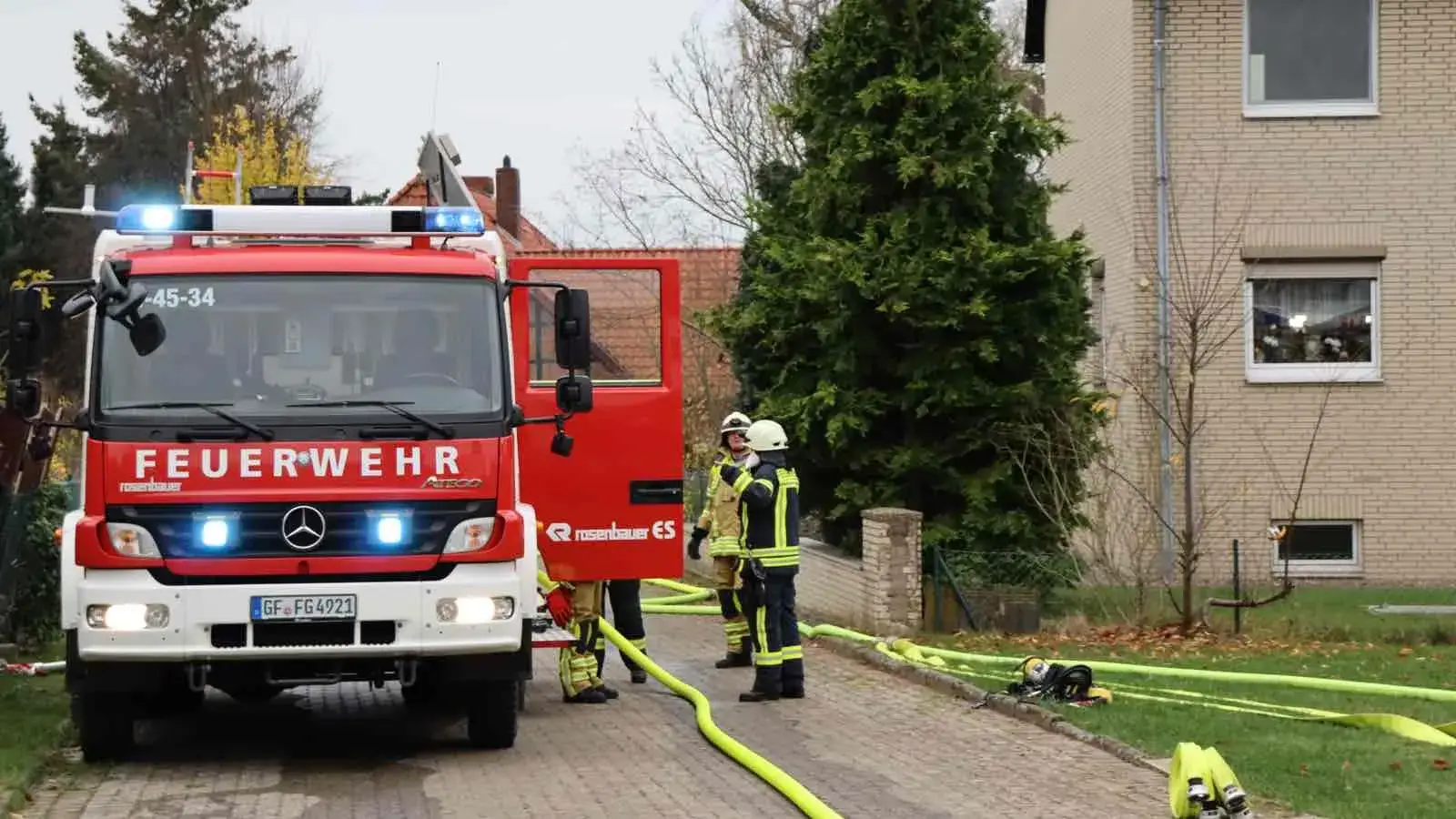 Eine Feuerwehrauto mit Feuerwehrleuten und ausgelegten Schläuchen vor einem Mehrfamilienhaus