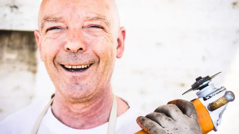 Ein lachender Mann, der eine kleine Flex in der Hand hält
