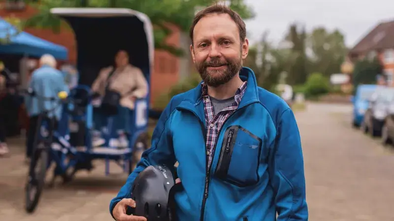 Ein Mann mit Jacke und Fahrradhelm steht vor einer Fahrrad-Rikscha.