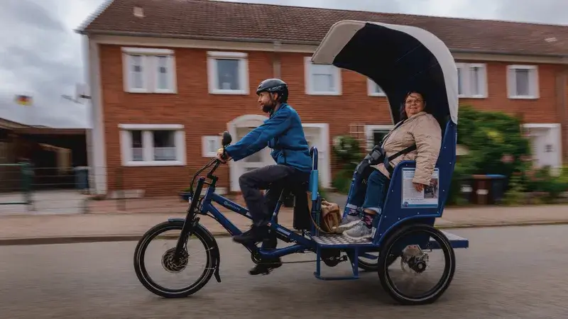 Eine Fahrrad-Rikscha mit einem Fahrer und einer Frau als Fahrgast fahren auf der Straße