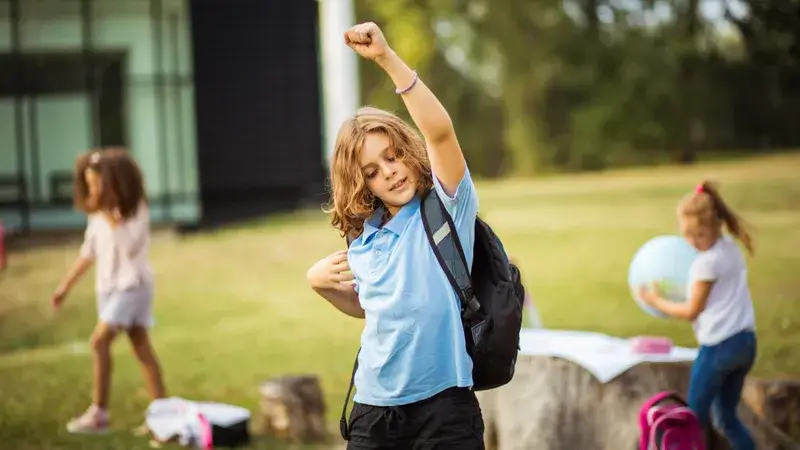 Drei Kinder mit Schulranzen spielen auf einer Wiese