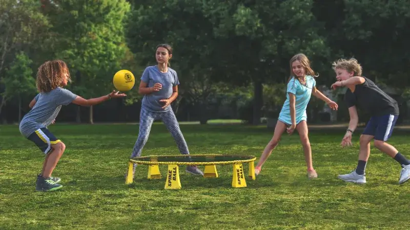 Vier Kinder spielen Spikeball auf einer Wiese.