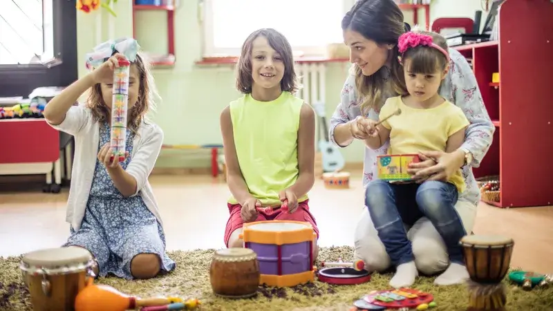 Eine Frau und drei Kinder sitzen in der Hocke und spielen mit perkussiven Instrumenten.