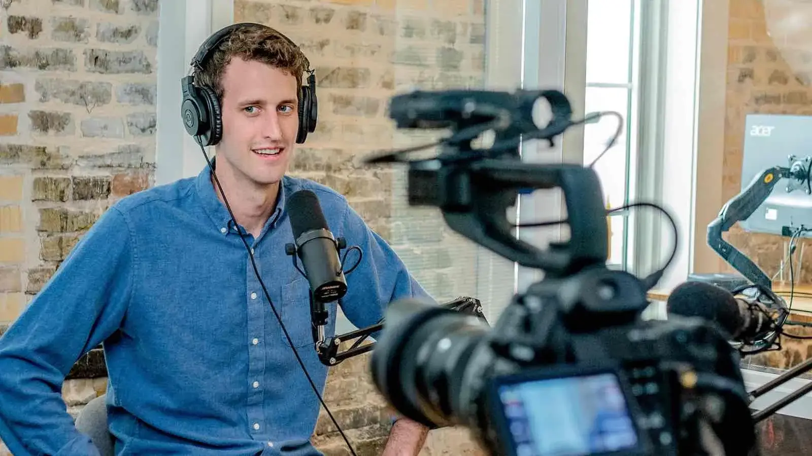 Ein Mann mit Headset und Mikrofon wird von einer Videokamera gefilmt.