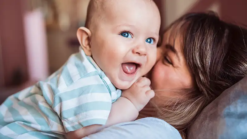 Ein lachendes Baby liegt auf dem Oberkörper seiner Mutter.