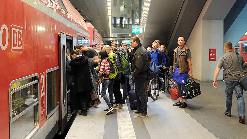 Menschen steigen in einen roten Zug der Deutschen Bahn an einem belebten Bahnsteig ein.