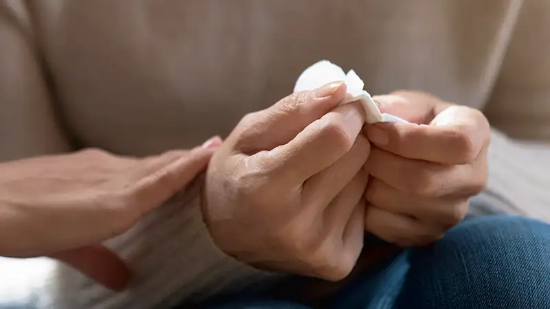 Eine Hand tröstet eine andere Person, die ein Taschentuch hält, Nahaufnahme auf die Hände.