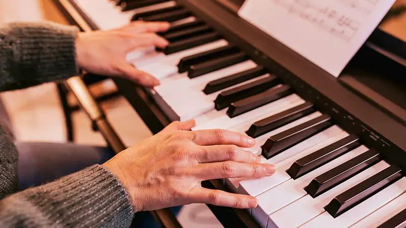 Nahaufnahme von Händen, die auf einem Klavier spielen, mit einem Notenblatt im Hintergrund.
