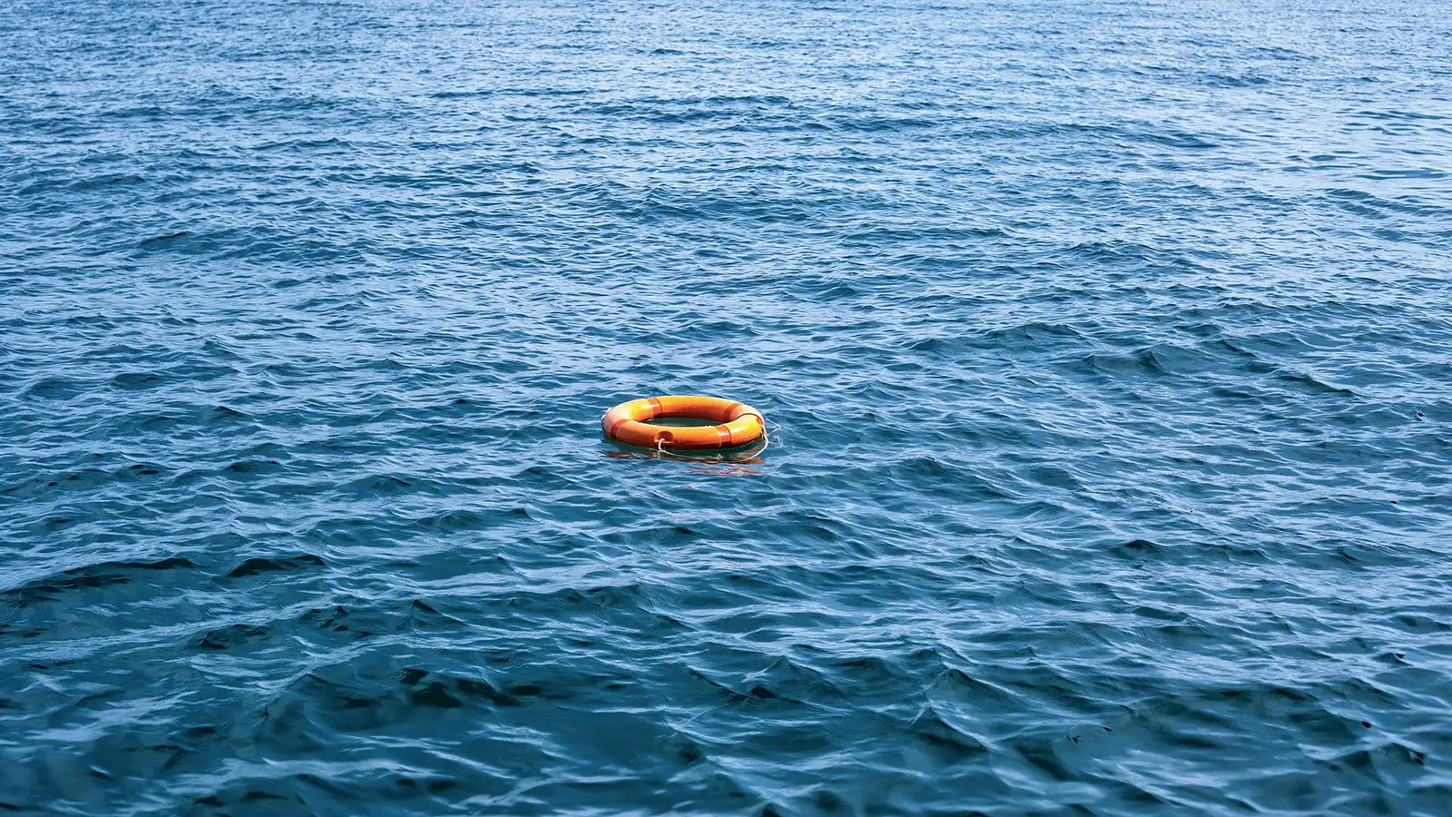 Ein einzelner oranger Rettungsring schwimmt auf der unruhigen Wasseroberfläche des Meeres.