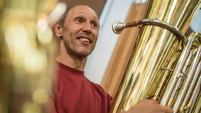 Ein lächelnder Mann spielt eine große Tuba in einem Innenraum.