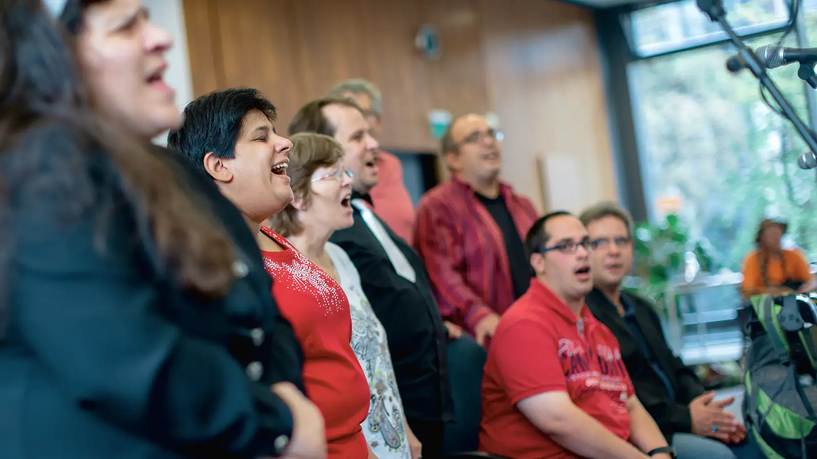 Eine Gruppe von Menschen unterschiedlichen Alters singt zusammen in einem Raum, einige sitzen, andere stehen.