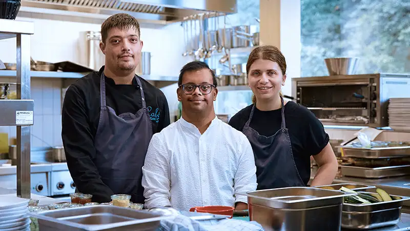 Drei Köche in einer professionellen Küche lächeln in die Kamera.