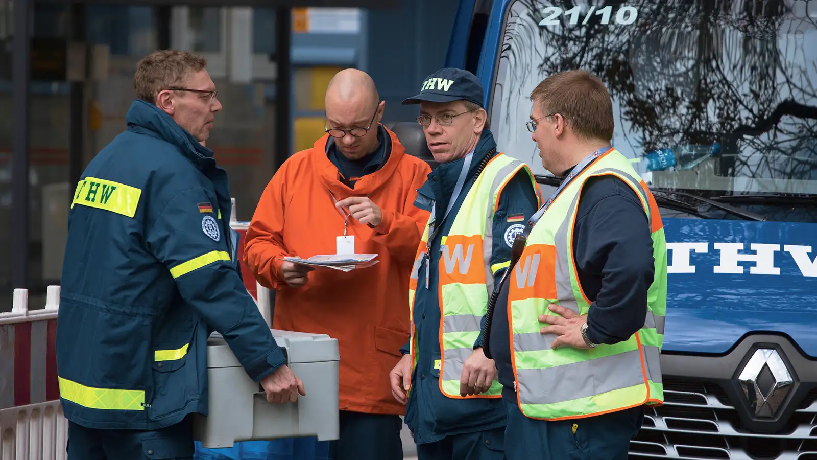 Vier Arbeiter in Warnwesten führen eine Besprechung vor einem LKW des Technischen Hilfswerks durch.