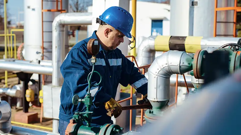 Ein Arbeiter mit blauem Schutzhelm überprüft Ventile in einer Industrieanlage.