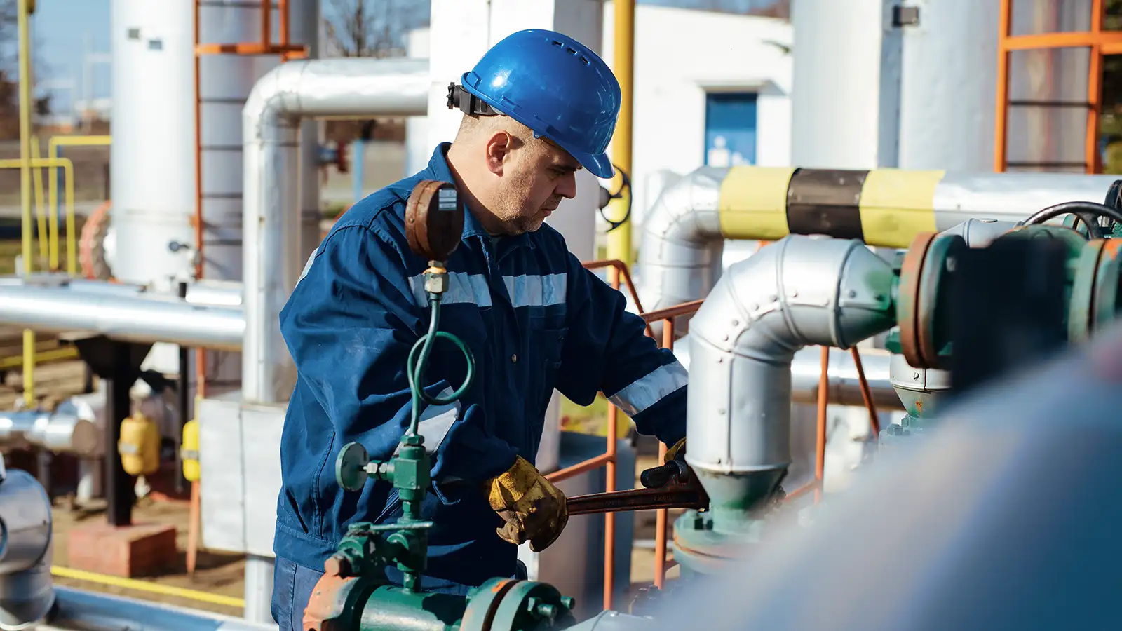 Ein Arbeiter mit blauem Schutzhelm überprüft Ventile in einer Industrieanlage.