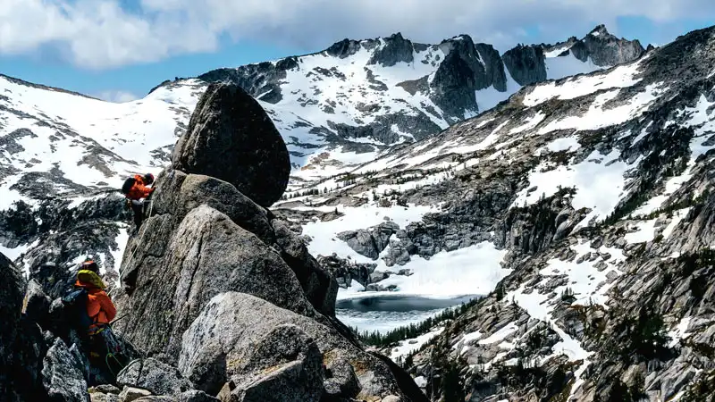 Bergsteiger in Rettungsausrüstung klettern auf einen Felsen am Berg mit Schneelandschaft im Hintergrund.