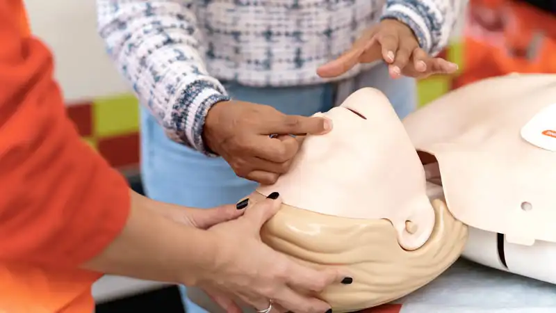Hände zeigen die korrekte Hand-Position an einer Erste-Hilfe-Puppe für Mund-zu-Mund-Beatmung.