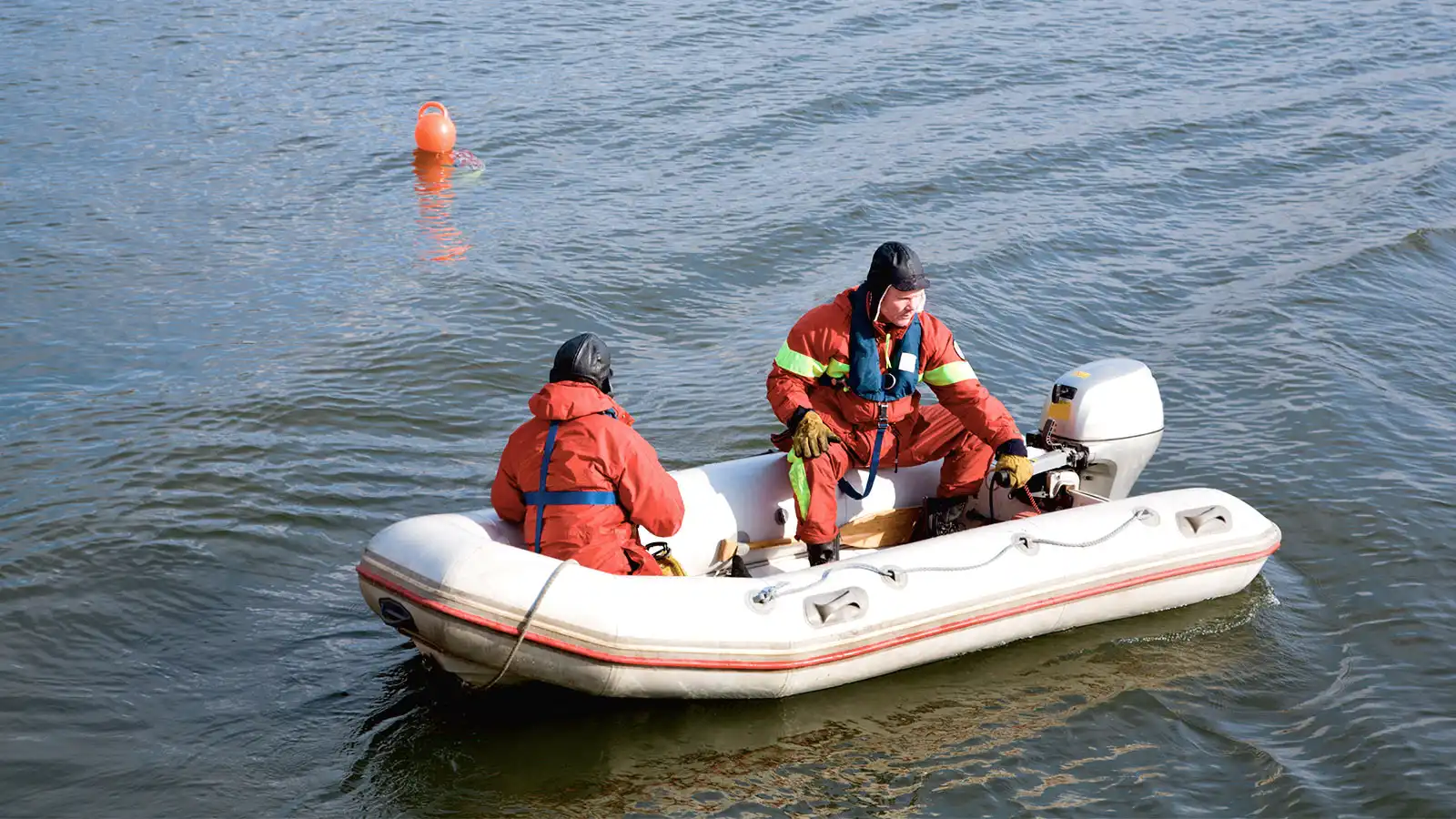 Zwei Personen in einem Schlauchboot mit Motor auf einem Gewässer.