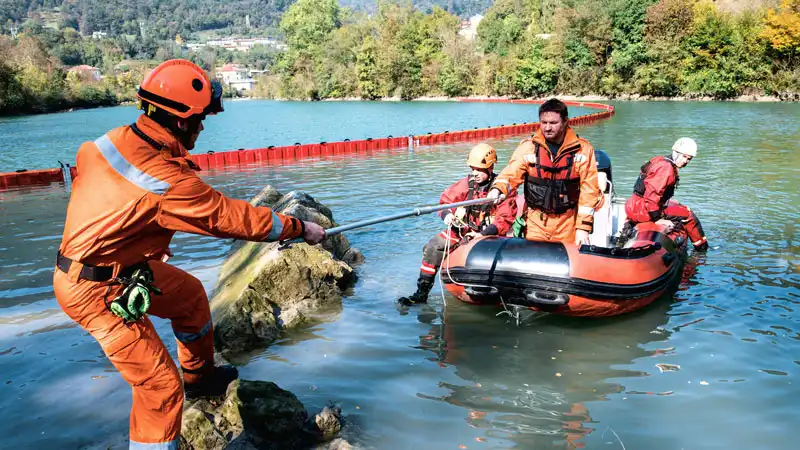 Rettungskräfte in einem Boot ziehen mit einem Seil an einem felsigen Ufer.