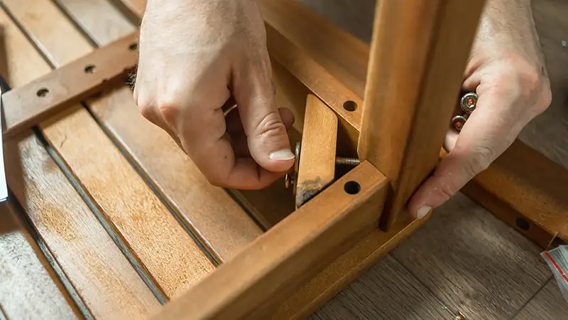 Zwei Hände montieren ein Holzstück an einem Möbelstück mit Schrauben.