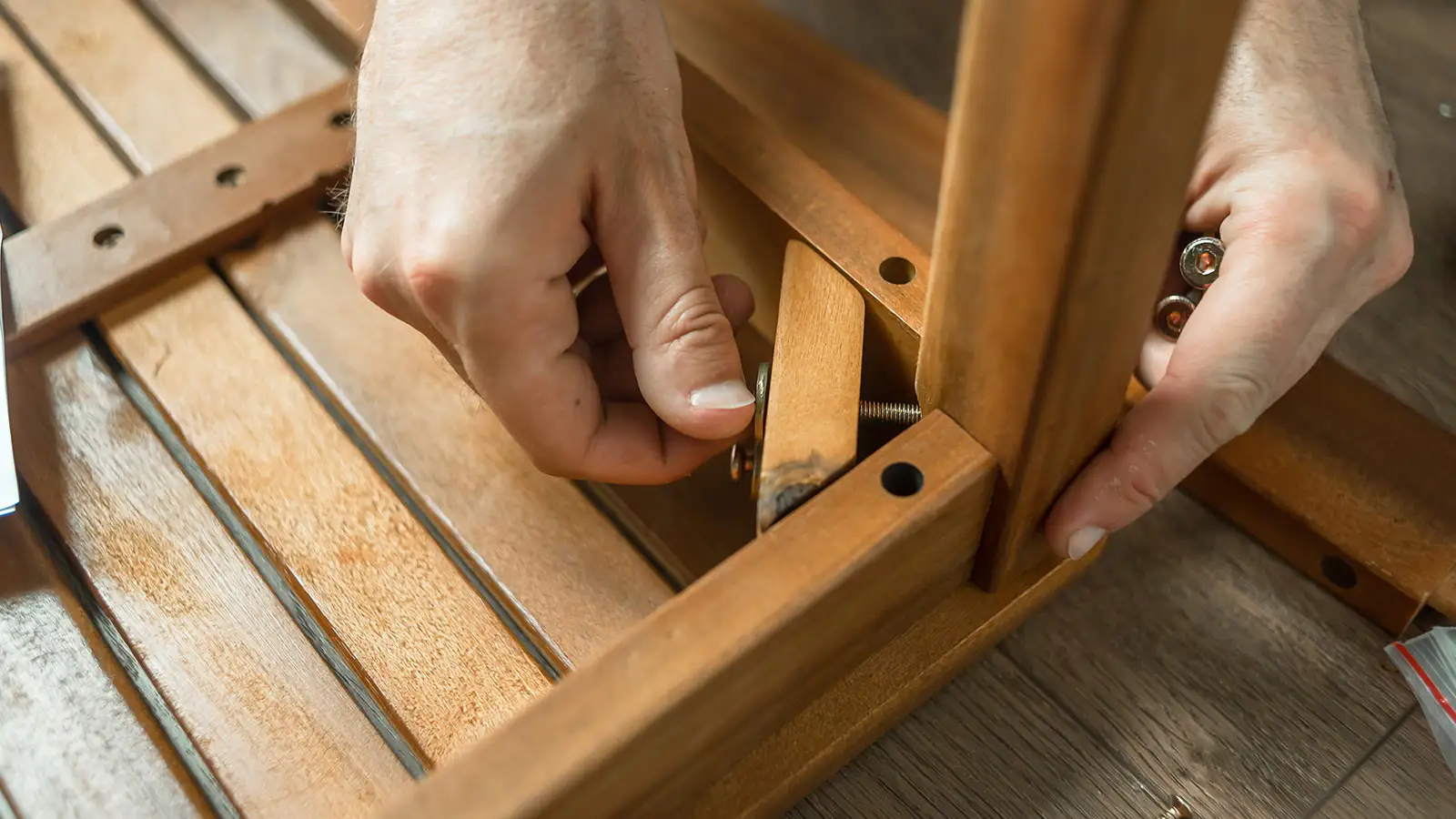 Zwei Hände montieren ein Holzstück an einem Möbelstück mit Schrauben.