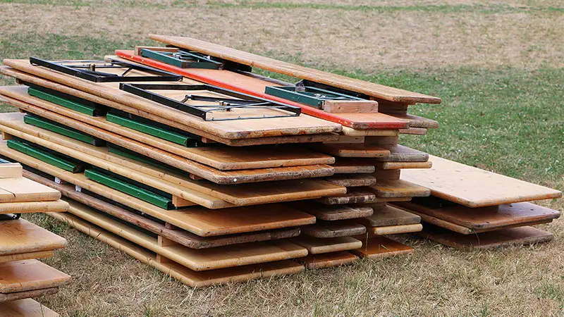 Stapel von Holztischen in verschiedenen Farben, darunter auch grüne und rote Tischbeine.