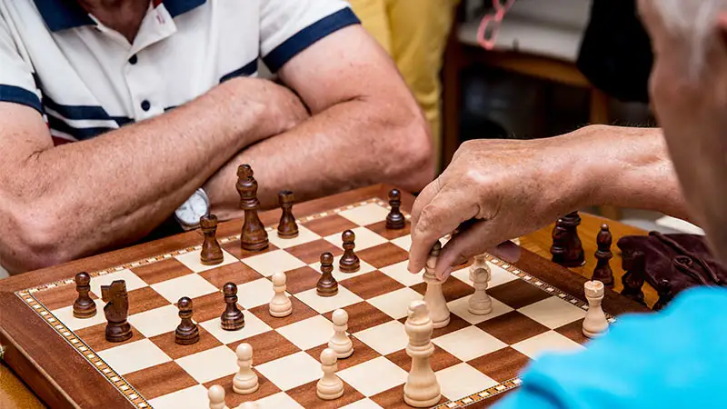 Zwei ältere Männer spielen Schach. Einer der Spieler bewegt gerade einen weißen Bauern.