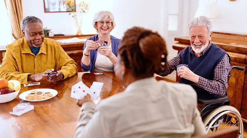 Vier ältere Menschen sitzen um einen Tisch und spielen Karten, während sie lachen und plaudern.