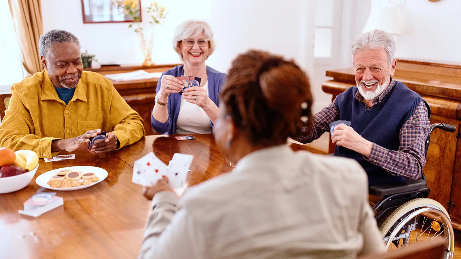 Vier ältere Menschen sitzen um einen Tisch und spielen Karten, während sie lachen und plaudern.