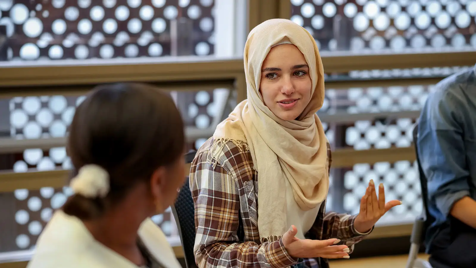 Eine Person trägt einen hellen Hijab und gestikuliert während eines Gesprächs mit einer anderen Person.