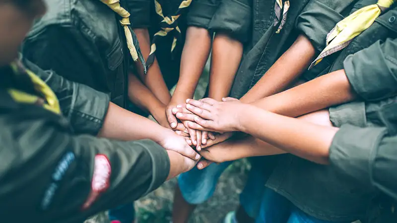 Kinder in Uniformen halten ihre Hände gemeinsam in der Mitte, symbolisierend für Teamwork und Zusammenhalt.