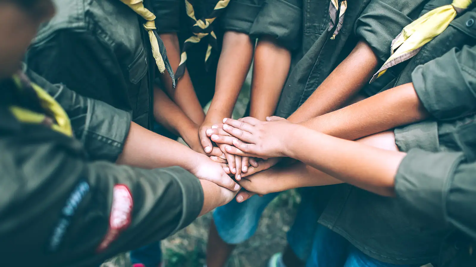 Kinder in Uniformen halten ihre Hände gemeinsam in der Mitte, symbolisierend für Teamwork und Zusammenhalt.